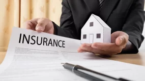Insurance agent showing insurance policy and holding a home on his hand.