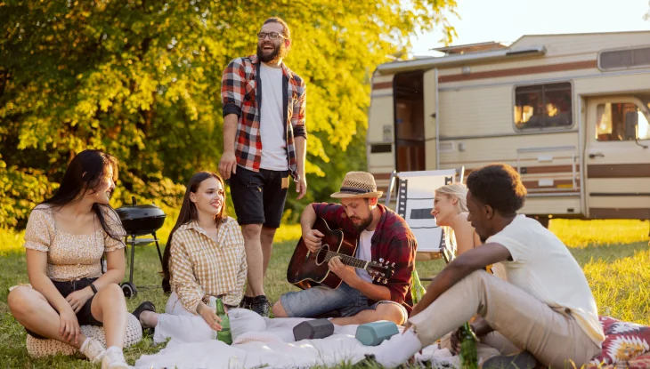 Group of friends play music and relax in front of RV.