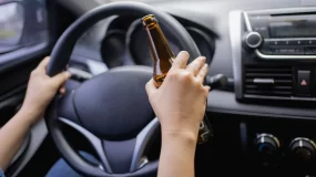 Man behind the wheel of a car with a bottle of beer.