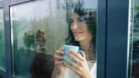 Woman drinking coffee looking out window at rain.