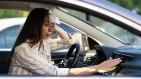 Pretty young woman feels hot air blowing out of air conditioner in car