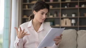 Stressed woman sitting on couch looking at home insurance contract.