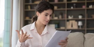 Stressed woman sitting on couch looking at home insurance contract.