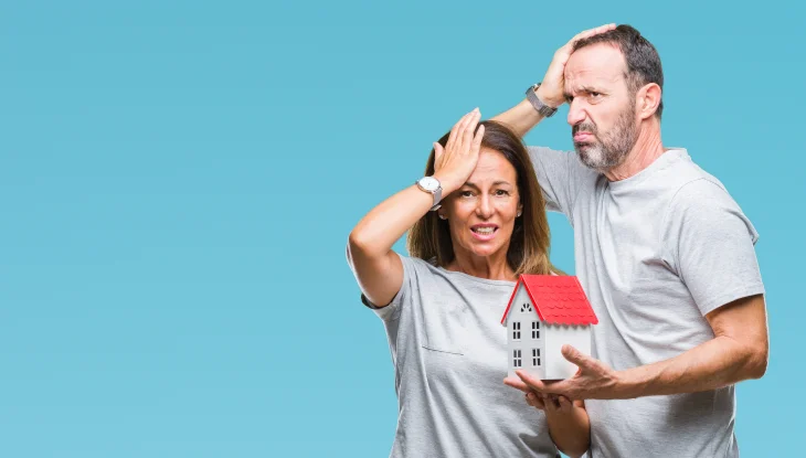 Stressed man and woman holding representation of home insurance.