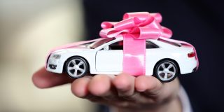 Toy car in a man's hand with a pink bow wrapped around it - car insurance in Georgia
