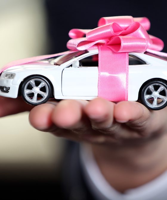 Toy car in a man's hand with a pink bow wrapped around it - car insurance in Georgia