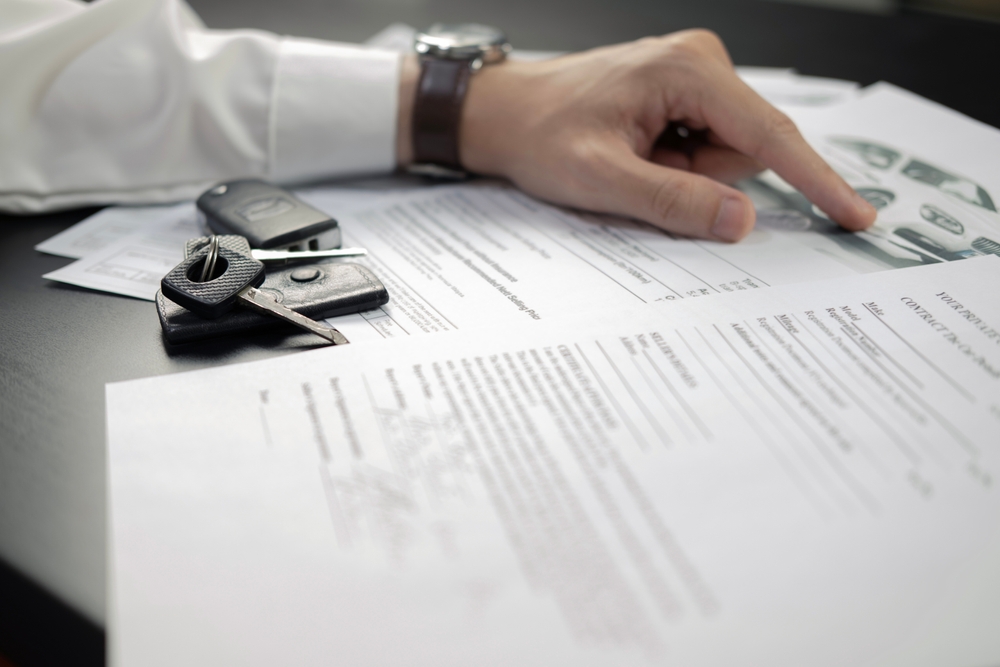 Man's hand pointing out features of a car on documents with car keys next to him - car insurance in Georgia
