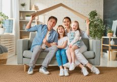Dada, mom and two children sit on couch under a replica of a roof to symbolize home protection - home insurance in Georgia