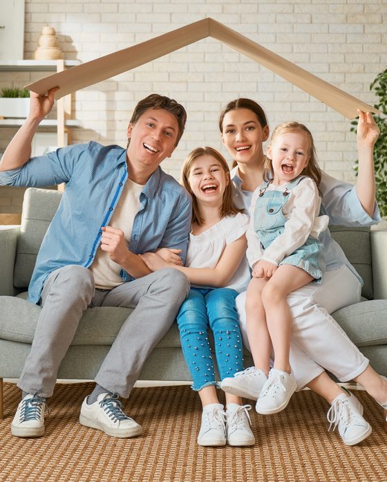 Dada, mom and two children sit on couch under a replica of a roof to symbolize home protection - home insurance in Georgia